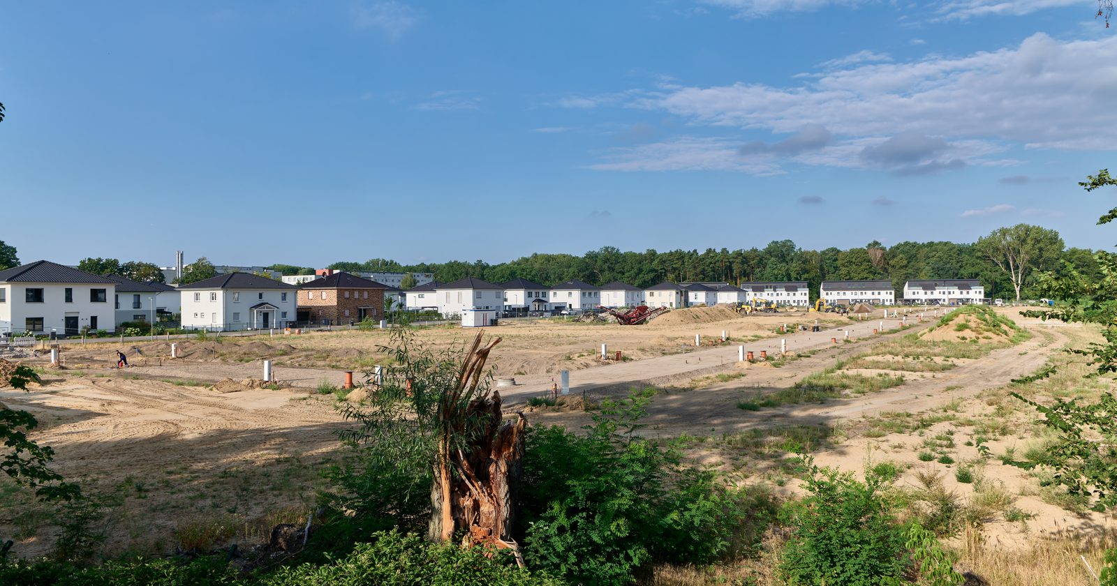 Plac budowy nowego osiedla mieszkaniowego z gotowymi domami w tle — budownictwo społeczne w toku